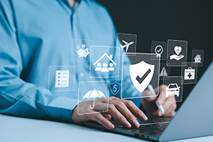 A professional in a blue shirt typing on a laptop, with digital insurance icons floating above, representing security, home, health, and travel coverage.